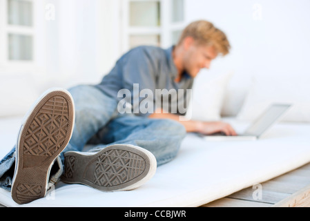 Man lying on bed using laptop computer Stock Photo