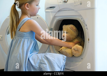 Little girl taking teddy bear out of dryer Stock Photo