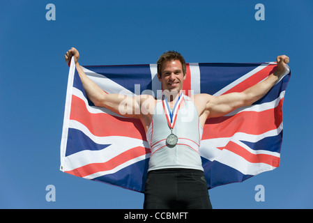 Male athlete on winner's podium, holding up British flag Stock Photo