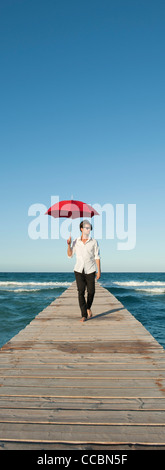 Young man walking on pier with umbrella Stock Photo