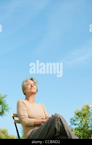 Senior woman sitting outdoors enjoying warmth of sun Stock Photo