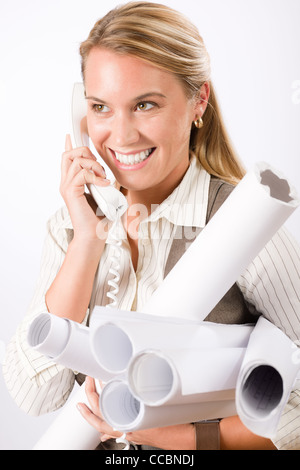 Smiling young female architect holding blueprints isolated on white background Stock Photo