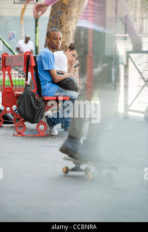 Young men sitting on bench watching person skateboarding Stock Photo