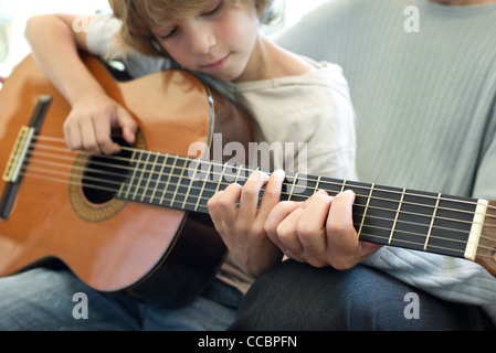 Boy learning how to play guitar with father