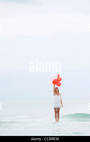 Woman standing on surface of water, holding bunch of balloons Stock Photo