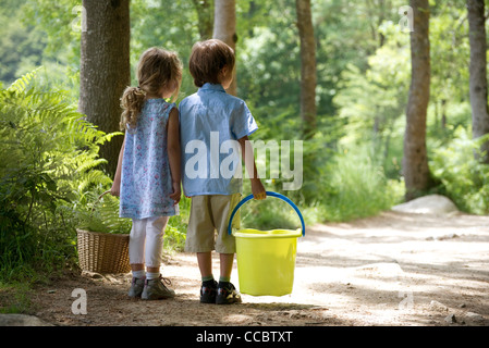 Children together on path in woods, girl carry basket and boy carrying bucket Stock Photo
