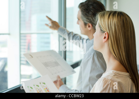 Colleagues looking holding blueprints and looking out window Stock Photo