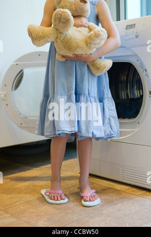 Girl standing in front of dryer, holding teddy bear Stock Photo