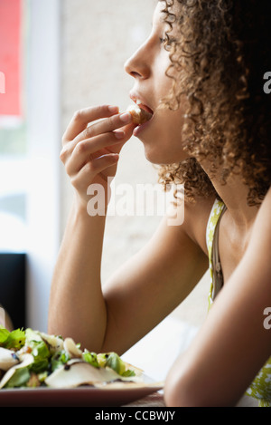 Young woman with curly hair eating salad, side view Stock Photo