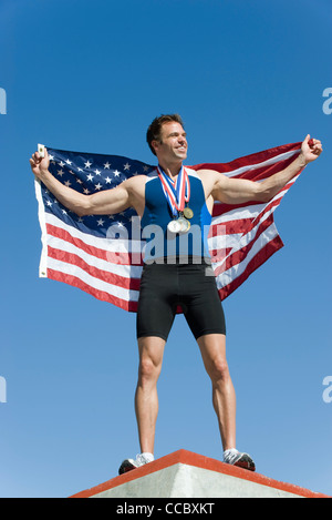 Male athlete on winner's podium, holding up American flag Stock Photo