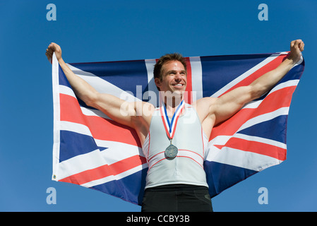 Male athlete on winner's podium, holding up British flag Stock Photo