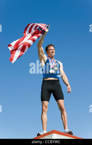 Male athlete on winner's podium, holding up American flag Stock Photo