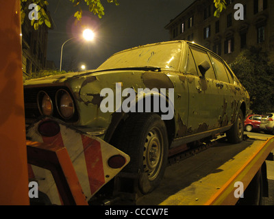 abandoned old damaged car on tow away truck lorry at night in city town Stock Photo