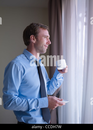 Mid adult business man relaxing and drinking a cup of tea, looking out of window. Side view Stock Photo