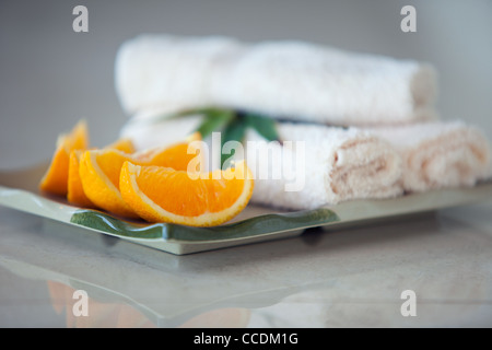 A line of freshly cut orange slices are arranged neatly next to a few warm and soft towels at a spa / resort Stock Photo