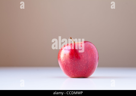 Single red apple on white table with taupe brown background. Stock Photo