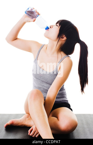 Chinese woman sitting on a yoga mat drinking water from a plastic bottle. Stock Photo