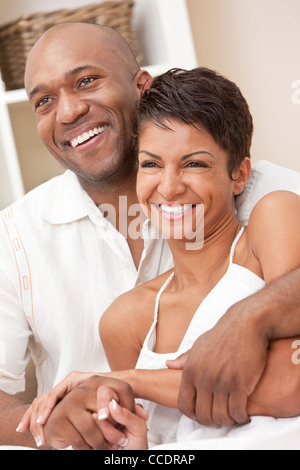 A happy African American man and woman couple in their thirties sitting at home together smiling. Stock Photo