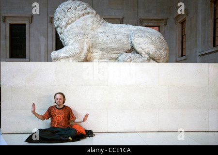A man performs qi gong exercises - part of a meditation flash mob in the Great Court of the British Museum beneath a lion statue Stock Photo