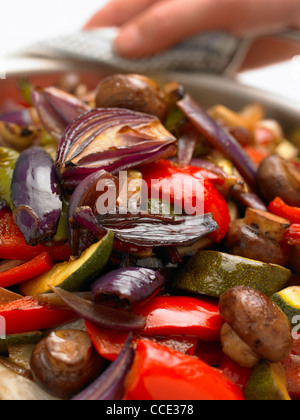 Roasted Vegetables in a serving pan with hand at back holding Stock Photo