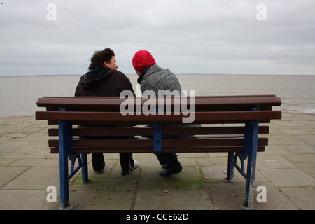 Two women sitting on a bench by the sea. Stock Photo