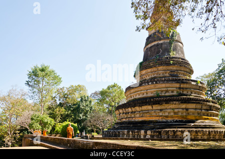 Buddhist monks in orange robes walk by stupa at Wat U Mong temple in Chiang Mai Thailand Stock Photo