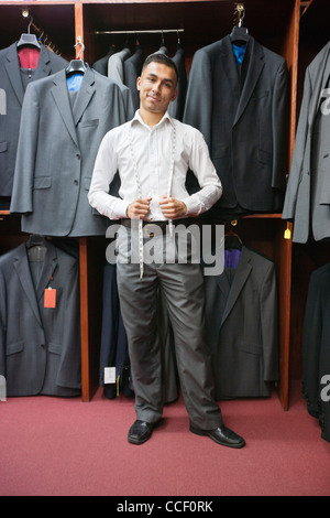 Portrait of young man posing with suits hanging in background Stock Photo