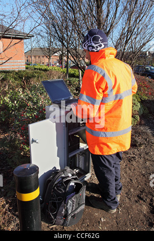 Technician wearing high vis jacket fixing roadside traffic monitor using a laptop computer. Stock Photo
