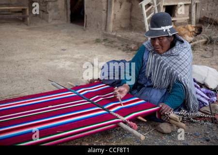 An Aymara woman weaves on a traditional hand loom in Huatajata on the Bolivian shore of Lake Titicaca. Stock Photo