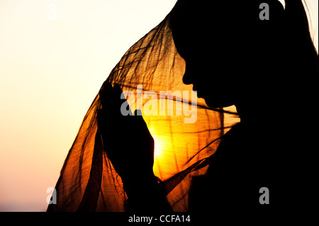 Indian teenage girl praying at sunset covered by a veil. Silhouette. India Stock Photo
