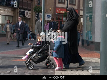 Oct 05, 2004; Leeds, UK; A muslim lady wearing a full length Burka covering everything except her eyes and her tennis shows walks in Leeds with her children and push chair stroller. There are large communities of Arabs, Indians and Asians living in the UK. Stock Photo