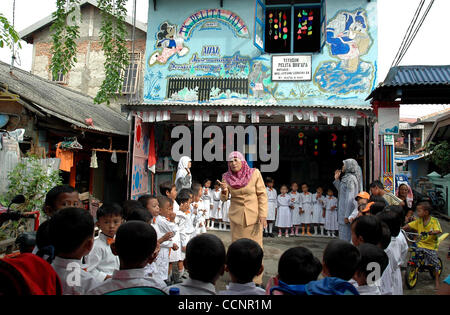JAKARTA,  INDONESIA  NOVEMBER 29, 2004    Endrizaemi, known as  'Ibu Haji', guides her students singing in front of an ex-garage they make as a school at Cilincing area. Besides working as the head of public elementary school, SD Negeri 03 Marunda, she also teaches in a school for the orphans and ab Stock Photo