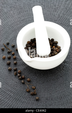 ceramic mortar and pestle full with aromatic black peppercorns Stock Photo