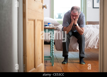 depressed senior male sitting on bed with head in hands Stock Photo