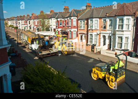 Resurfacing a long suburban street, two yellow road rollers and tar layer shot from high vantage point. Brightly coloured. Stock Photo