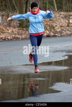 2 young women running in winter, jumping over wet spots on the way. Stock Photo