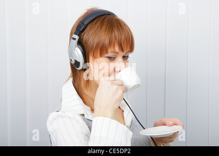 The girl in headphones with a microphone drinks coffee Stock Photo