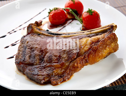 Club Steak. Veal on the bone. Grilled meat ribs on white plate with cherry tomatoes and dark hot sauce