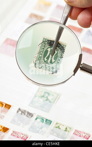 Man holding postage stamps from collection with tweezers under magnifying glass Stock Photo