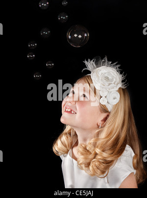 An attractive girl looks up as bubbles fall all around her. Stock Photo