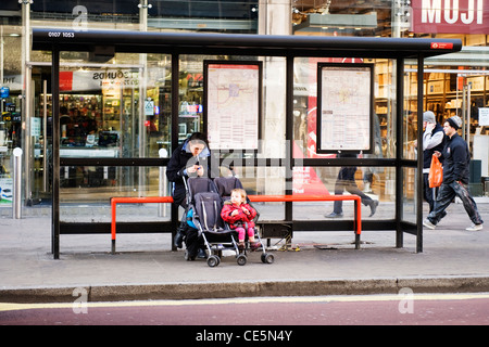 Charing Cross Road Tottenham Court Road West End London young mother sitting bus stop toddler pushchair buggy smoking street scene shops stores Stock Photo