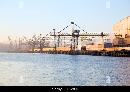 Sea port cranes in the bank of the river Nervion, in Bilbao, during dawn, next to the scrap yard of a steel mill Stock Photo