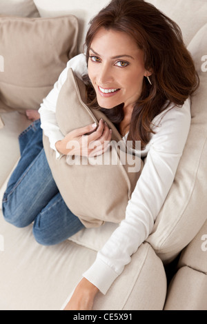 Overhead photograph of beautiful young woman at home sitting on sofa or settee holding a cushion and smiling Stock Photo