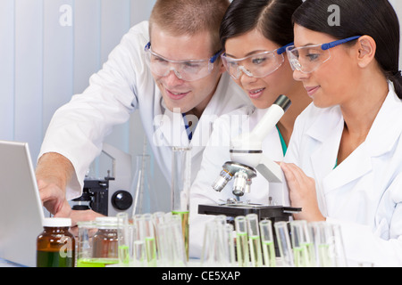 Interracial team of male and female medical or scientific researchers or doctors using a laptop & microscope in a laboratory. Stock Photo