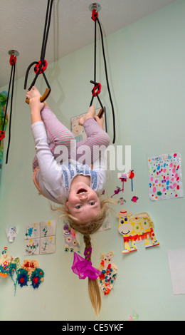 A 7-years old girl hanging on gymnastic rings in her home room. Stock Photo