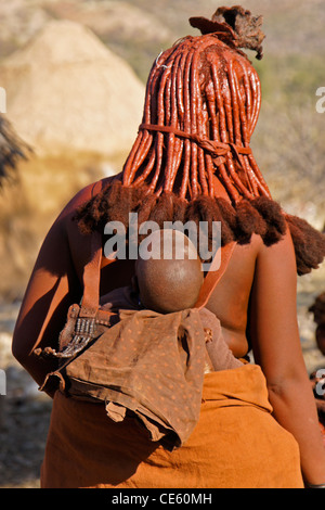 Himba woman with baby on back, village near Opuwo, Namibia Stock Photo