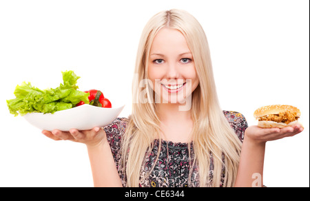 thoughtful young woman holding a hamburger with chicken and plate with vegetables, isolated against white background Stock Photo