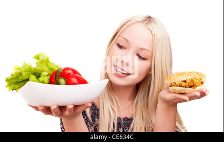thoughtful young woman holding a hamburger with chicken and plate with vegetables, isolated against white background Stock Photo
