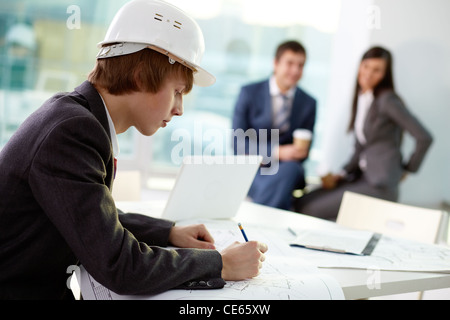 Young engineer working in office with his colleagues on background Stock Photo