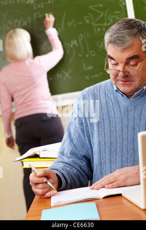 Portrait of mature man making notes on background of teacher writing on blackboard Stock Photo